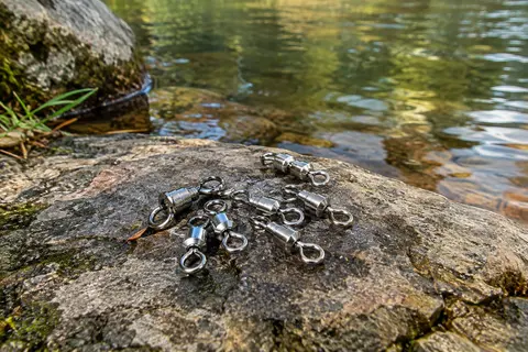 Émerillons rolling en acier inoxydable à finition nickelée posés sur une pierre au bord de l’eau