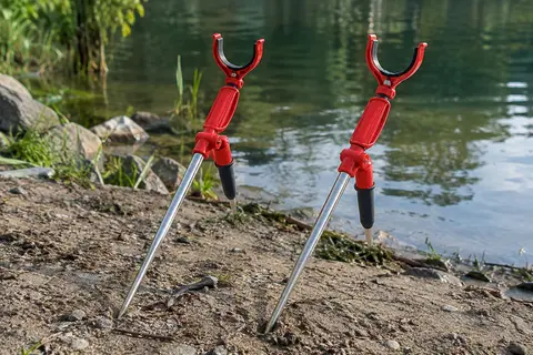 Deux supports rouges pour cannes à pêche avec tiges en acier inoxydable posés près d’une rive
