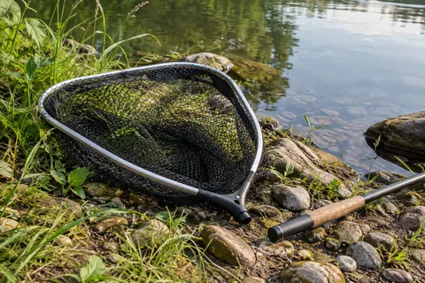 Tête d’épuisette Lineaeffe en aluminium avec filet noir, posée au bord d’une rivière calme