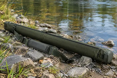 Étui de canne à mouche en toile vert militaire avec tube rigide et bandoulière, posé près d’une rive calme.