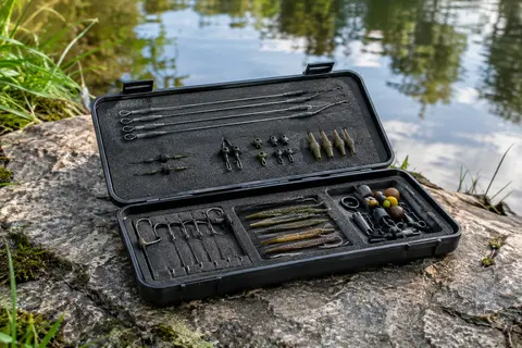 Boîte de pêche noire ouverte avec mousse, broches et accessoires de montage au bord d’une rivière