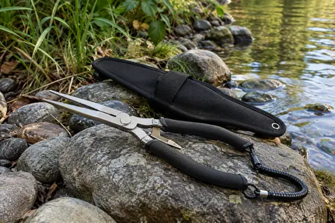 Pince de pêche noire à bec long avec sa gaine en nylon, posée sur une rive calme
