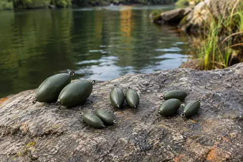 Huit plombs ovales vert mat de quatre masses différentes posés sur une pierre au bord de l’eau