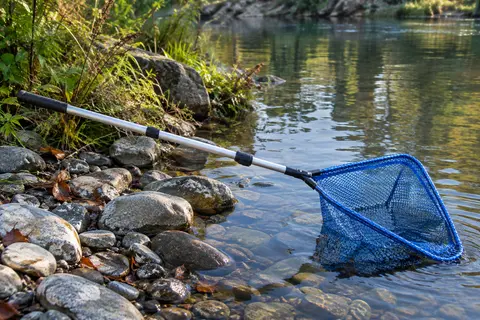 Épuisette pliable bleue à manche télescopique et filet caoutchouté posée au bord d’une rivière