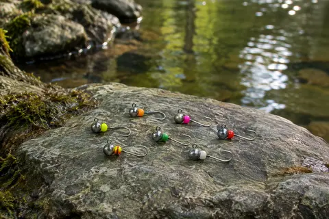 Petites têtes plombées en tungstène aux perles vives et hameçons argentés, posées au bord de l’eau